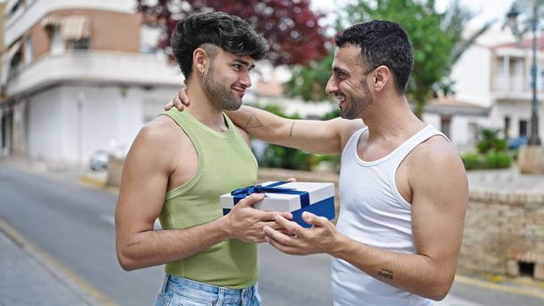 Dwóch mężczyzn para uśmiechnięta pewna siebie niespodzianka z prezentem urodzinowym na ulicy - Zdjęcie, obraz