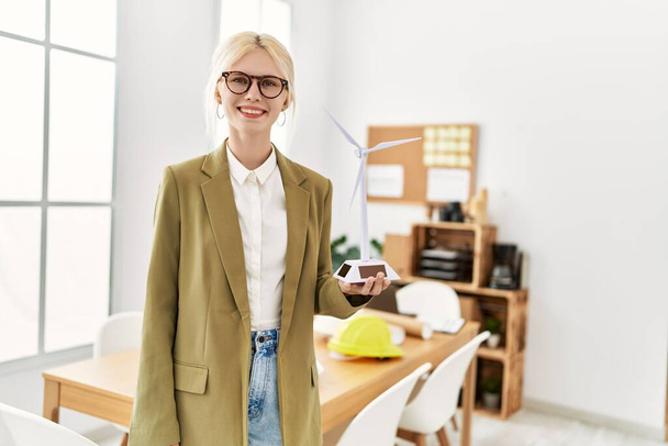 Fiatal szőke nő építész mosolygós magabiztos gazdaság szélmalom az irodában - Fotó, kép