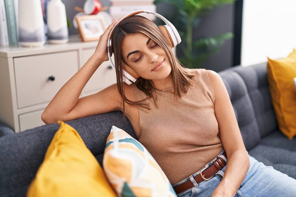 Młoda, piękna latynoska kobieta słuchająca muzyki siedzącej na kanapie w domu - Zdjęcie, obraz