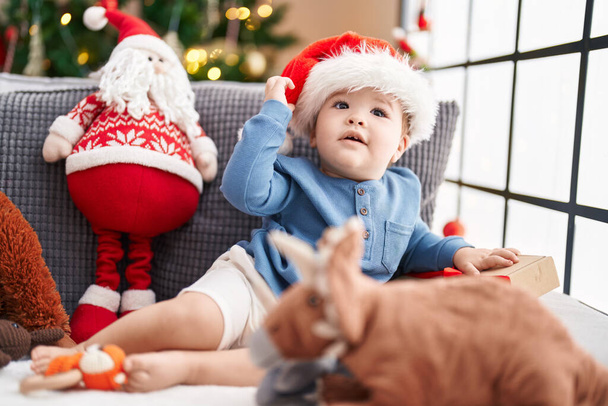 Adorabile bambino caucasico sdraiato sul divano vicino all'albero di Natale con espressione rilassata a casa - Foto, immagini