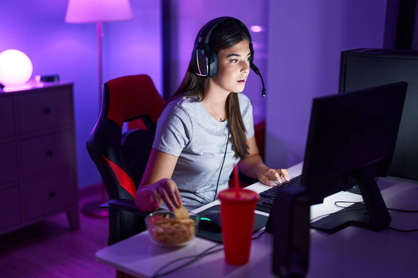 Fiatal gyönyörű spanyol nő streamer videojáték eszik chips-et a játékteremben - Fotó, kép