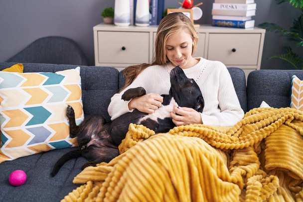 Young blonde woman hugging dog sitting on sofa at home - Foto, Imagen