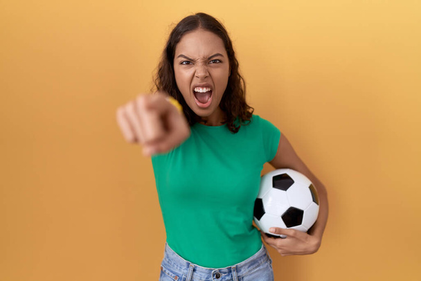 Молодая латиноамериканка, держащая мяч, указывая недовольным и разочарованным на камеру, злая и злая на тебя  - Фото, изображение