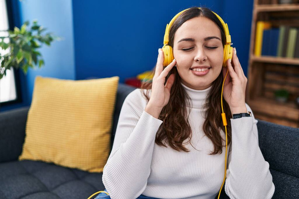 Молода красива іспаномовна жінка слухає музику, сидячи на дивані вдома
 - Фото, зображення