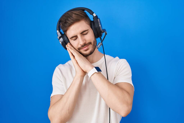 Spanyol férfi szakállal zenét hallgat fejhallgatóban alszik fáradt álmodozás és pózol kéz a kézben, miközben mosolyog csukott szemmel.  - Fotó, kép