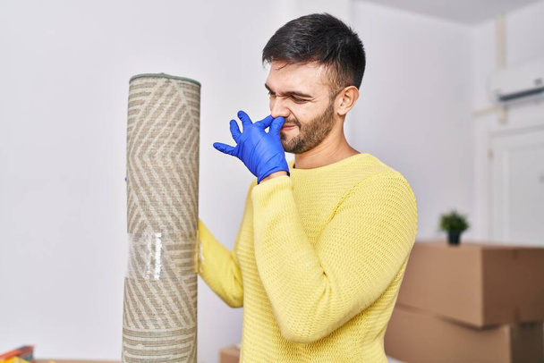 Young hispanic man smelling dirty carpet at new home - Фото, зображення