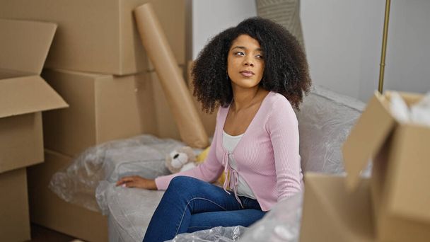 Mujer afroamericana sentada en un sofá con expresión relajada en un nuevo hogar - Foto, Imagen