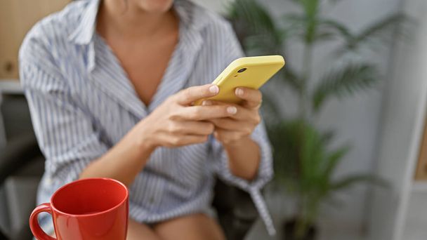 Sikeres spanyol női munkás kezei, akik üzenetet gépelnek a telefonján, belemerülnek a munkába az irodájában, miközben megkóstolnak egy csésze eszpresszót, és otthon ülnek. - Fotó, kép