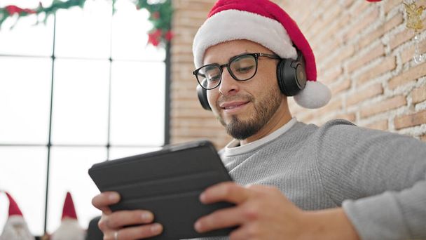 自宅でクリスマスの装飾で音楽を聴くタッチパッドを使用したヒスパニック男性 - 写真・画像