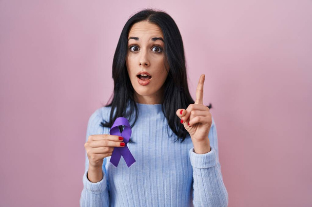 Latino nainen tilalla violetti nauha tietoisuutta yllättynyt idea tai kysymys sormella onnellinen kasvot, numero yksi  - Valokuva, kuva