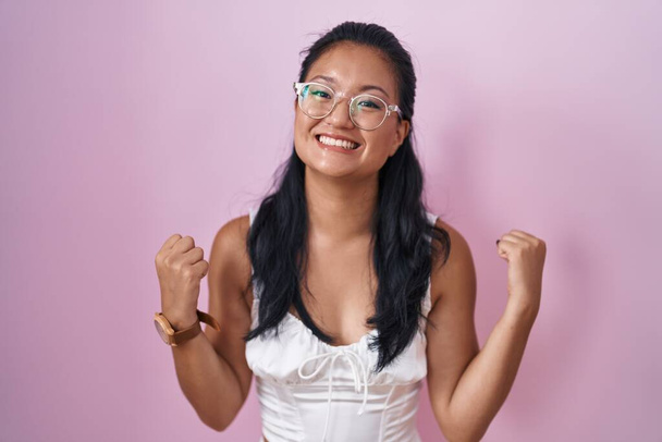 Asiatique jeune femme debout sur fond rose criant fier, célébrant la victoire et le succès très excité avec les bras levés  - Photo, image
