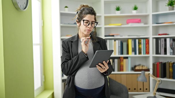 Jonge zwangere vrouw leraar met behulp van touchpad op bibliotheek universiteit - Foto, afbeelding