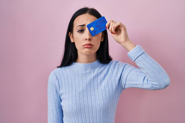 Latynoska kobieta trzymająca kartę kredytową nad okiem przygnębiona i martwiąca się o niepokój, płacząca wściekła i przerażona. smutna ekspresja.  - Zdjęcie, obraz