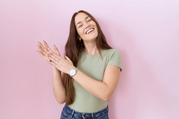 Beautiful brunette woman standing over pink background clapping and applauding happy and joyful, smiling proud hands together  - Photo, Image