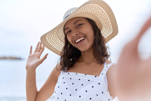 Young african american woman wearing summer hat make selfie by camera at seaside - Foto, imagen