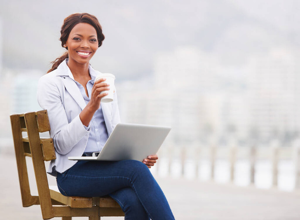 Black business woman, coffee and laptop on bench, promenade and portrait with smile, drink and beach. Entrepreneur, happy and outdoor with tea cup, computer and nature by ocean with fog in Cape Town. - Foto, Imagen