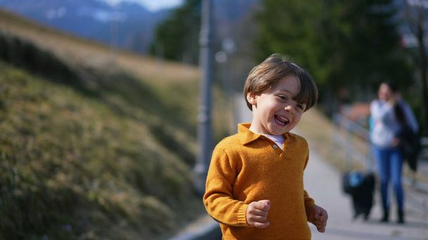Radosny, podekscytowany chłopczyk wybiegający na zewnątrz jesienią w żółtym pulowerze. Zbliżenie twarzy dziecka w ruchu sprinting do przodu uczucie beztroski - Zdjęcie, obraz