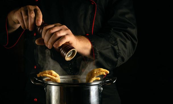 Csirkelábat sütni egy étterem konyhájában. A szakács száraz borsot ad a forró serpenyőhöz. Fekete hely a reklámozáshoz - Fotó, kép