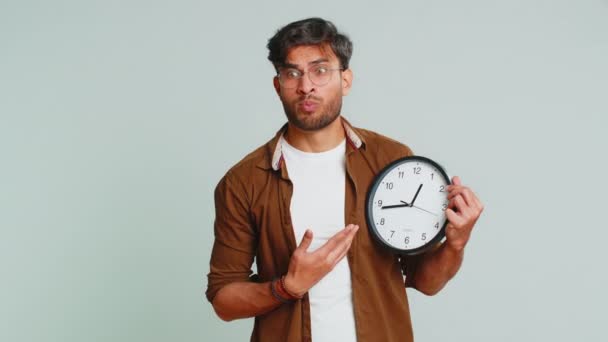 Indian young man with anxiety checking time on clock, running late to work, being in delay, deadline. Arabian guy looking at hour, minutes, worrying to be punctual isolated on studio gray background - Footage, Video