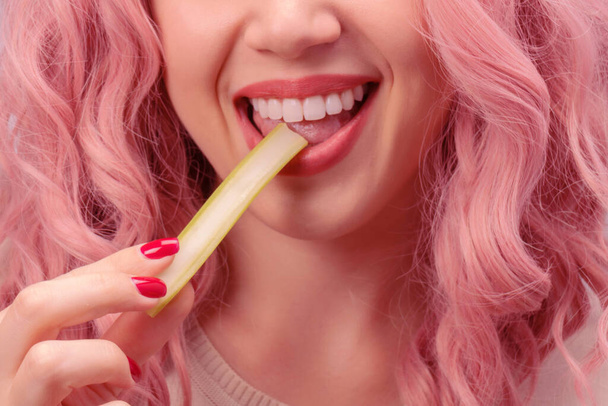 Selderij steekt in een vrouwenhand. vrouw met roze krullend haar is eten selderij close-up.  - Foto, afbeelding