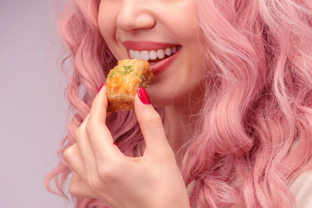 Mujer con el pelo rizado rosa está comiendo baklava primer plano. - Foto, imagen