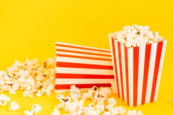 Rode en witte gestreepte dozen met popcorn en decoratieve pompoenen op een gele achtergrond. Entertainment concept. Herfst Film avond met popcorn. Herfst Cinema thema. - Foto, afbeelding