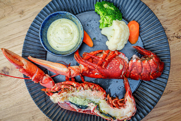 Un gros plan de moitiés de homard rouge délicieusement bouillies servies sur une assiette noire élégante dans un restaurant gastronomique. La chair de homard succulente est parfaitement cuite et prête à être dégustée. - Photo, image