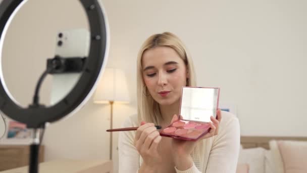 Young woman making beauty and cosmetic tutorial video content for social media. Beauty blogger using camera and light ring while showing how to apply eyeshadow to audience or follower. Blithe - Footage, Video