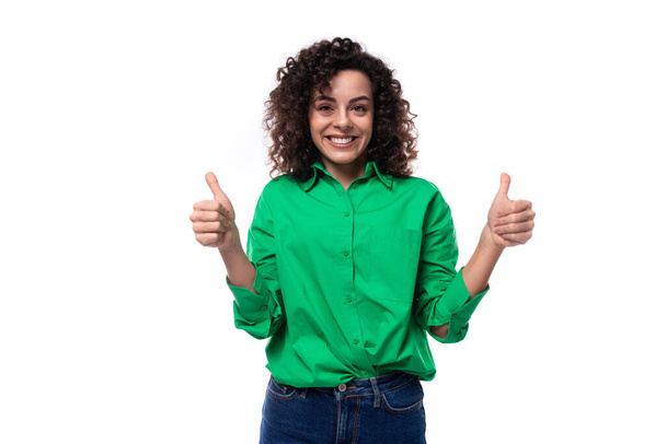 joven mujer morena europea sonriente brillante con un estilo rizado en una camisa verde trabaja en una agencia de publicidad. - Foto, imagen