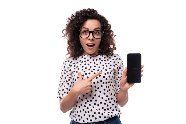 молодая стильная белая женщина с кудрявой завивкой показывает телефон с макетом. - Фото, изображение