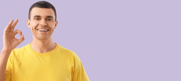 Knappe glimlachende jonge man tonen OK op lila achtergrond met ruimte voor tekst - Foto, afbeelding