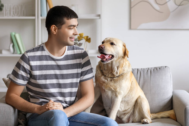 Mladý muž s labradorským psem sedí doma na pohovce - Fotografie, Obrázek
