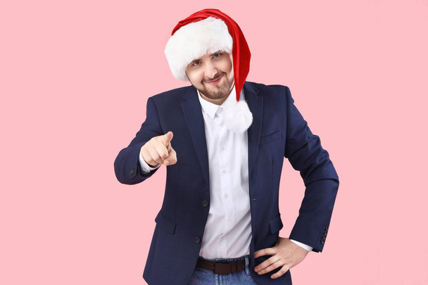 Junger Mann mit Weihnachtsmütze zeigt auf Betrachter auf rosa Hintergrund - Foto, Bild
