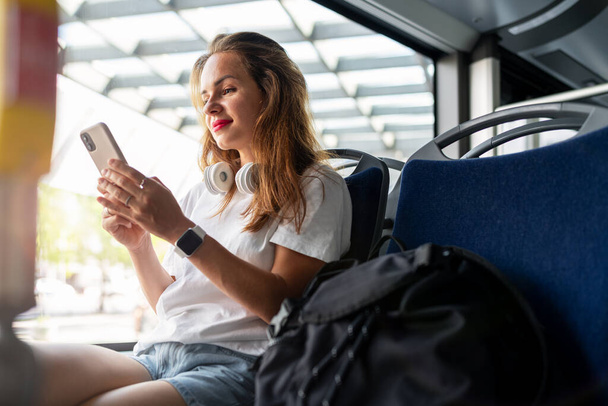 Genç kadın otobüste oturuyor ve akıllı telefonunu kullanıyor. Şehir ulaşımı ve yolcu. - Fotoğraf, Görsel