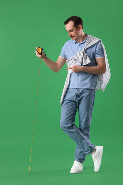 Young man with tape measure on green background - Foto, Imagen