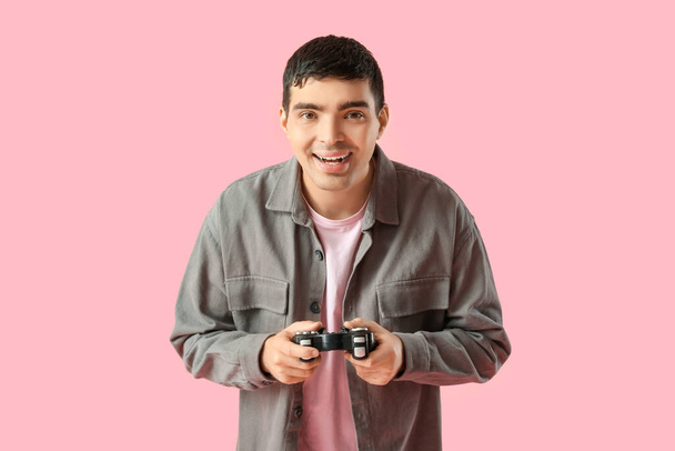 Ευτυχισμένος νεαρός άνδρας με pad παιχνίδι σε ροζ φόντο - Φωτογραφία, εικόνα