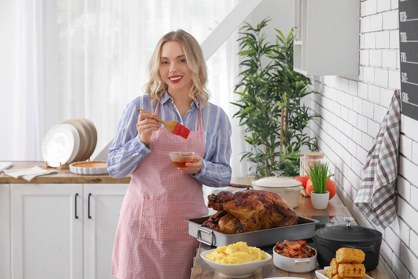 Hermosa joven mujer preparando sabroso pavo horneado en la mesa en la cocina. Celebración del Día de Acción de Gracias - Foto, Imagen