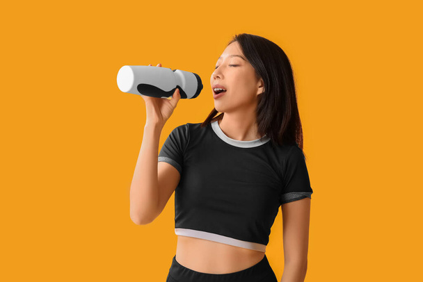 Beautiful young Asian woman with bottle of water on yellow background. Weight loss concept - Photo, Image