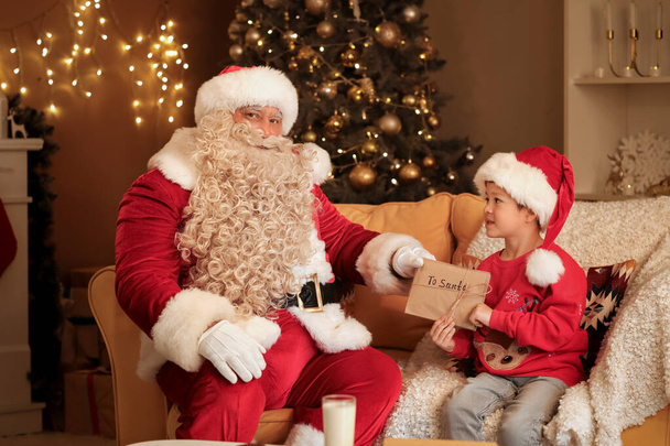 Санта Клаус и милый маленький мальчик с письмами дома в канун Рождества - Фото, изображение
