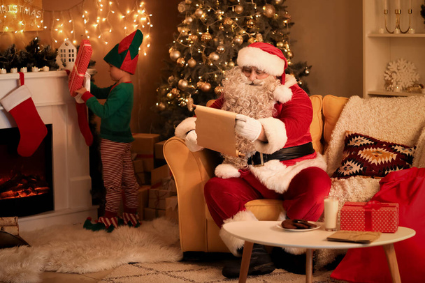 Weihnachtsmann liest Brief mit süßem Wichtelmännchen an Heiligabend - Foto, Bild