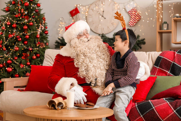 Kerstman en schattig jongetje in rendieren hoorns thuis op kerstavond - Foto, afbeelding