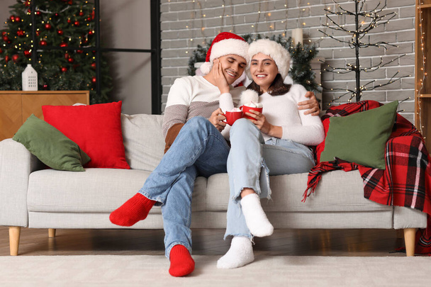 Ευτυχισμένο νεαρό ζευγάρι πίνοντας ζεστό κακάο με ζαχαρωτά στο σπίτι την παραμονή των Χριστουγέννων - Φωτογραφία, εικόνα