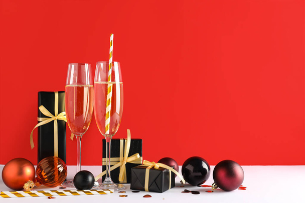 Композиция с бокалами шампанского, рождественскими подарками и украшениями на красном фоне - Фото, изображение
