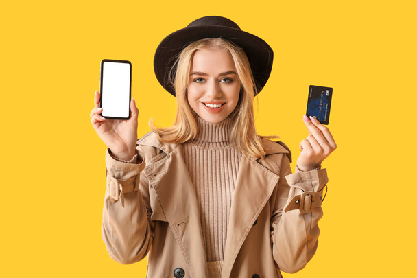 Sarı arka planda modern cep telefonu ve kredi kartı olan genç bir kadın. - Fotoğraf, Görsel