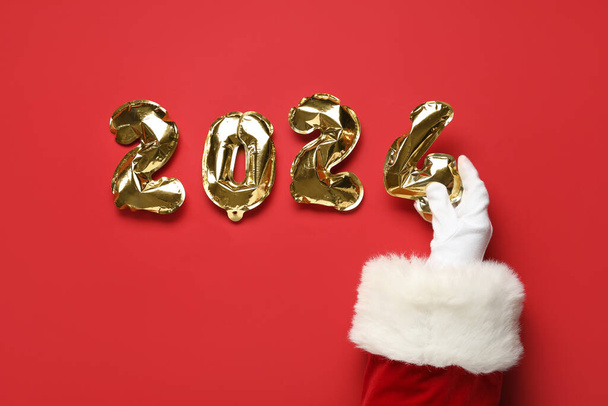 Santa hand with figure 2024 made of foil balloons on red background, closeup - Photo, Image