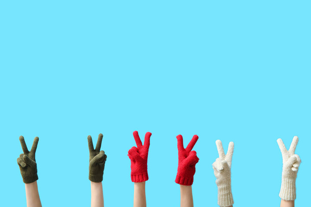Manos femeninas con guantes cálidos mostrando el gesto de victoria sobre el fondo de color - Foto, Imagen