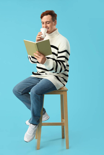 Młody człowiek pijący kawę i czytający książkę na kolorowym tle - Zdjęcie, obraz