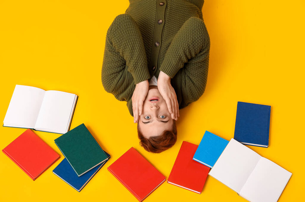 Emocionální muž ležící na žlutém pozadí s různými knihami - Fotografie, Obrázek