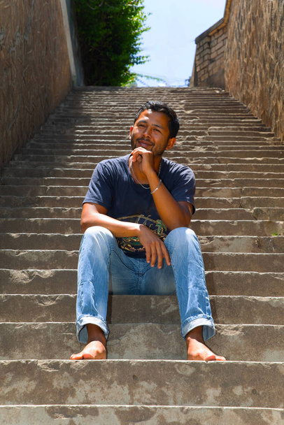 zbliżenie portret młody przystojny Malgaski facet uśmiecha się, siedzi na schodach, mówi telefon. - Zdjęcie, obraz