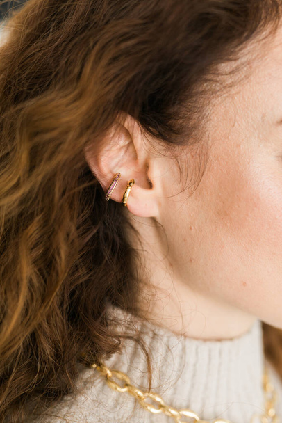 Recortado primer plano de una joven con dos asimétricas orejeras doradas. Mujer con orejeras doradas, vista lateral - Foto, Imagen
